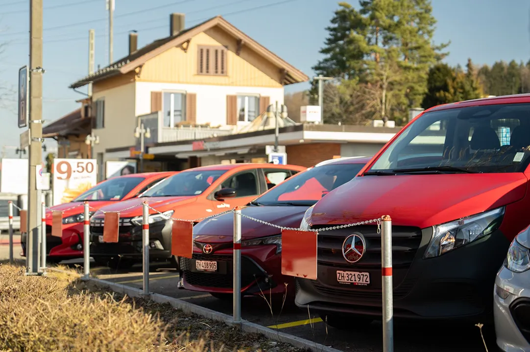Rangée de véhicules de car sharing sur des places de parc devant une gare, dans une zone rurale.