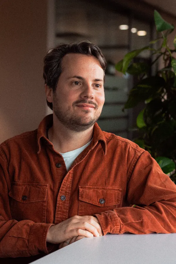 Markus Broder est assis à un bureau et regarde sur le côté en souriant.