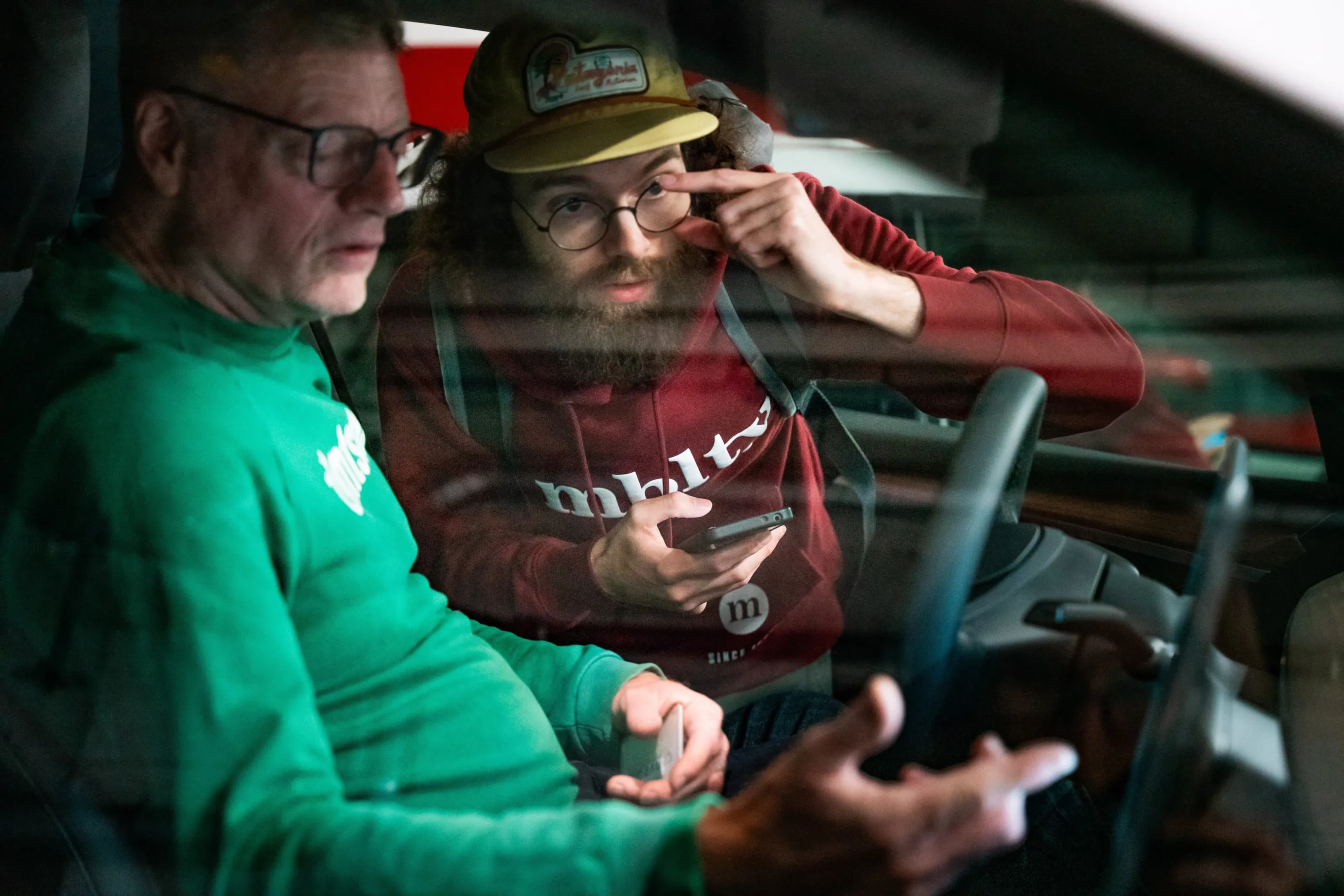 Deux hommes assis dans une voiture regardent un smartphone pendant une discussion.
