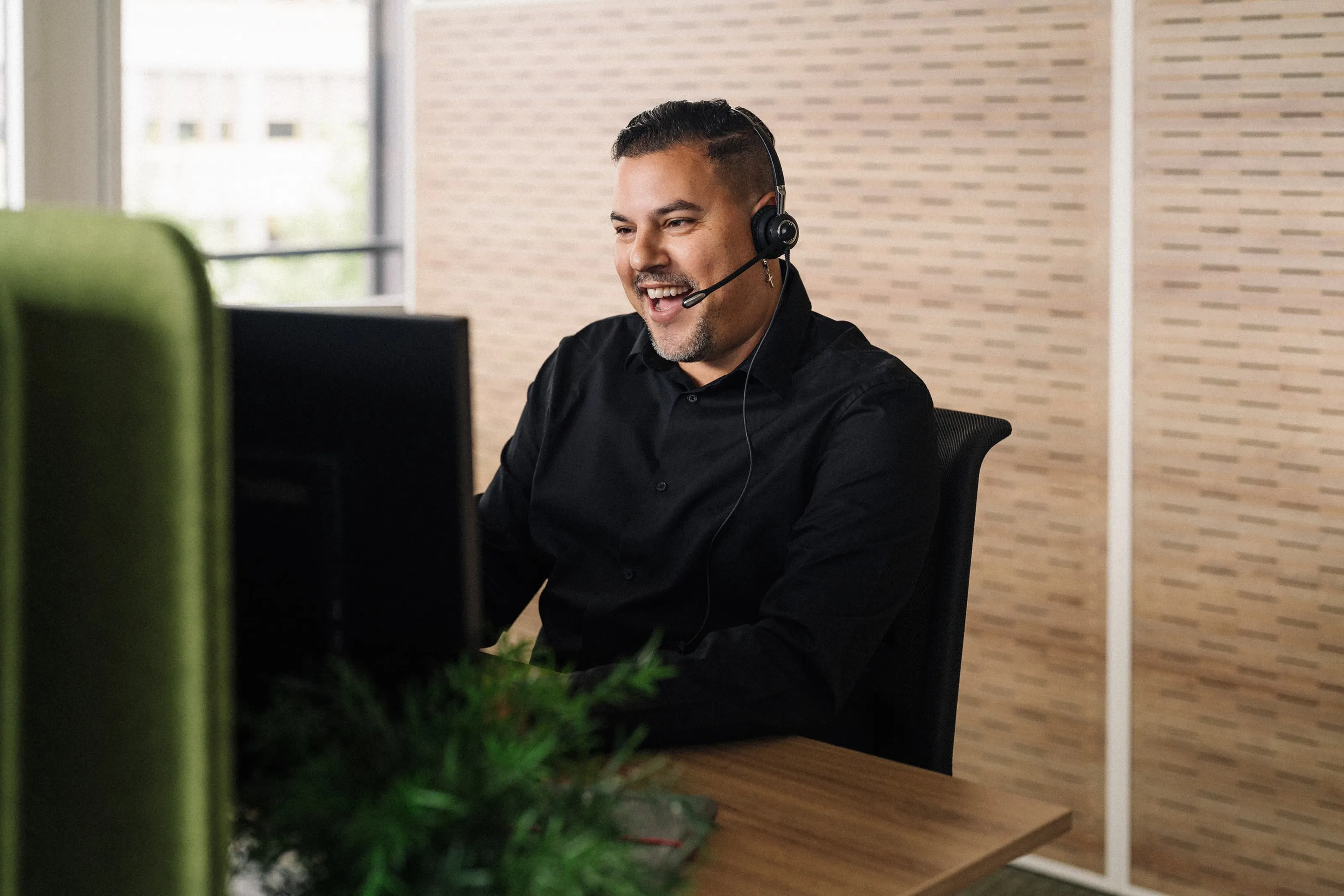 Équipé d’un casque, Ricardo Perrini est assis au bureau devant un écran et parle en souriant pendant un entretien avec un client.